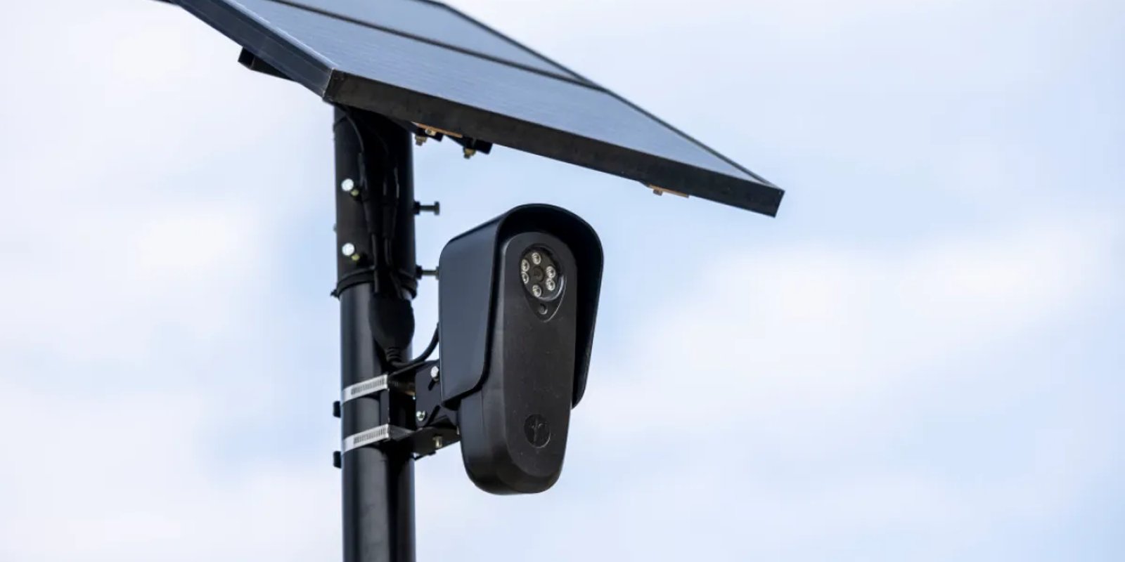 A solar-panel-topped automated license plate reader camera mounted on a pole against an overcast sky