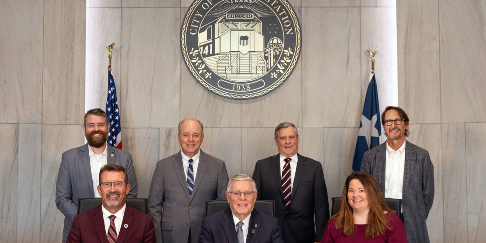 Members of the College Station City Council posed in council chambers beneath the City of College Station seal