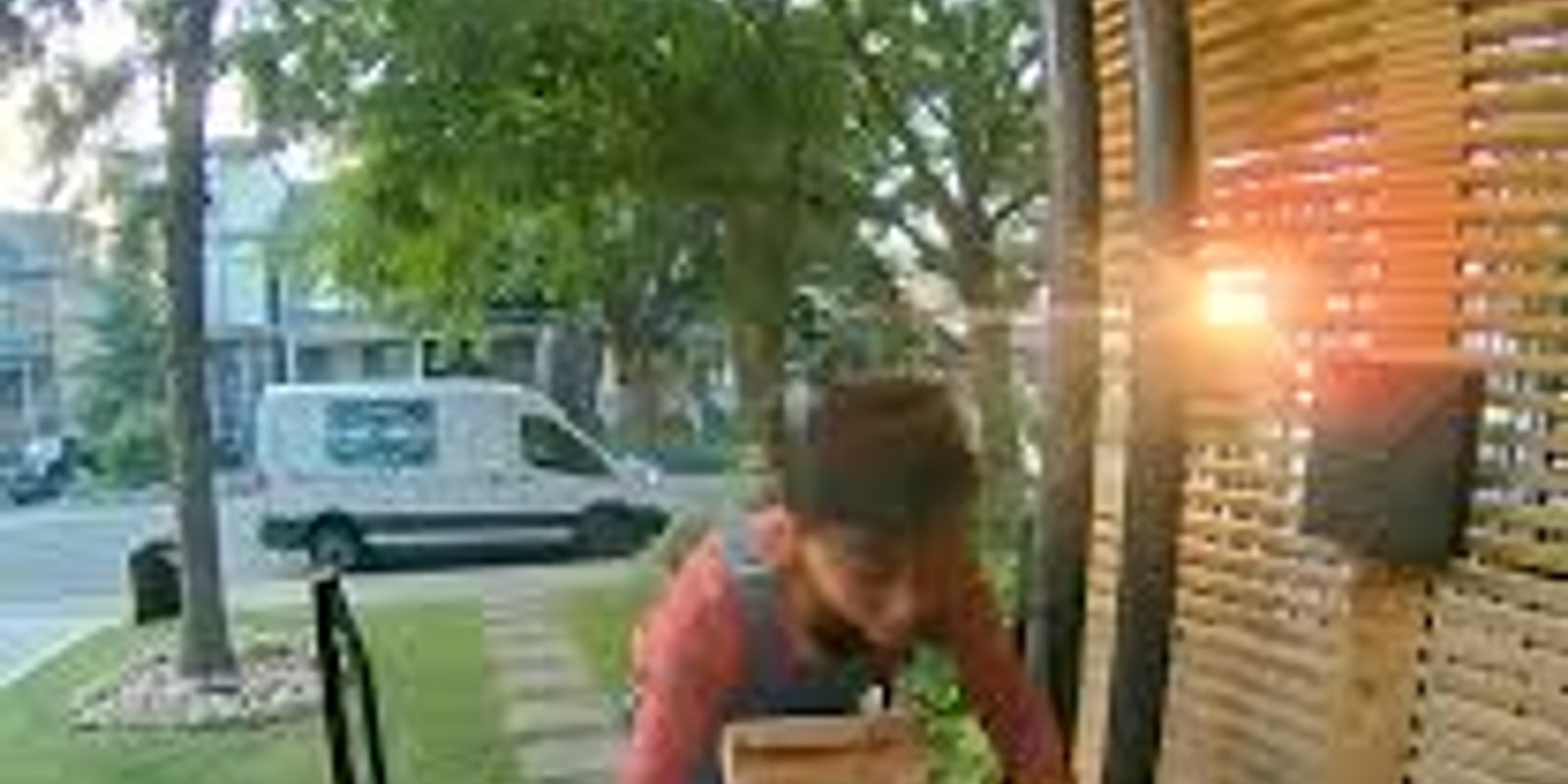 A doorbell camera view of a child carrying a crate of vegetables onto a wooden porch
