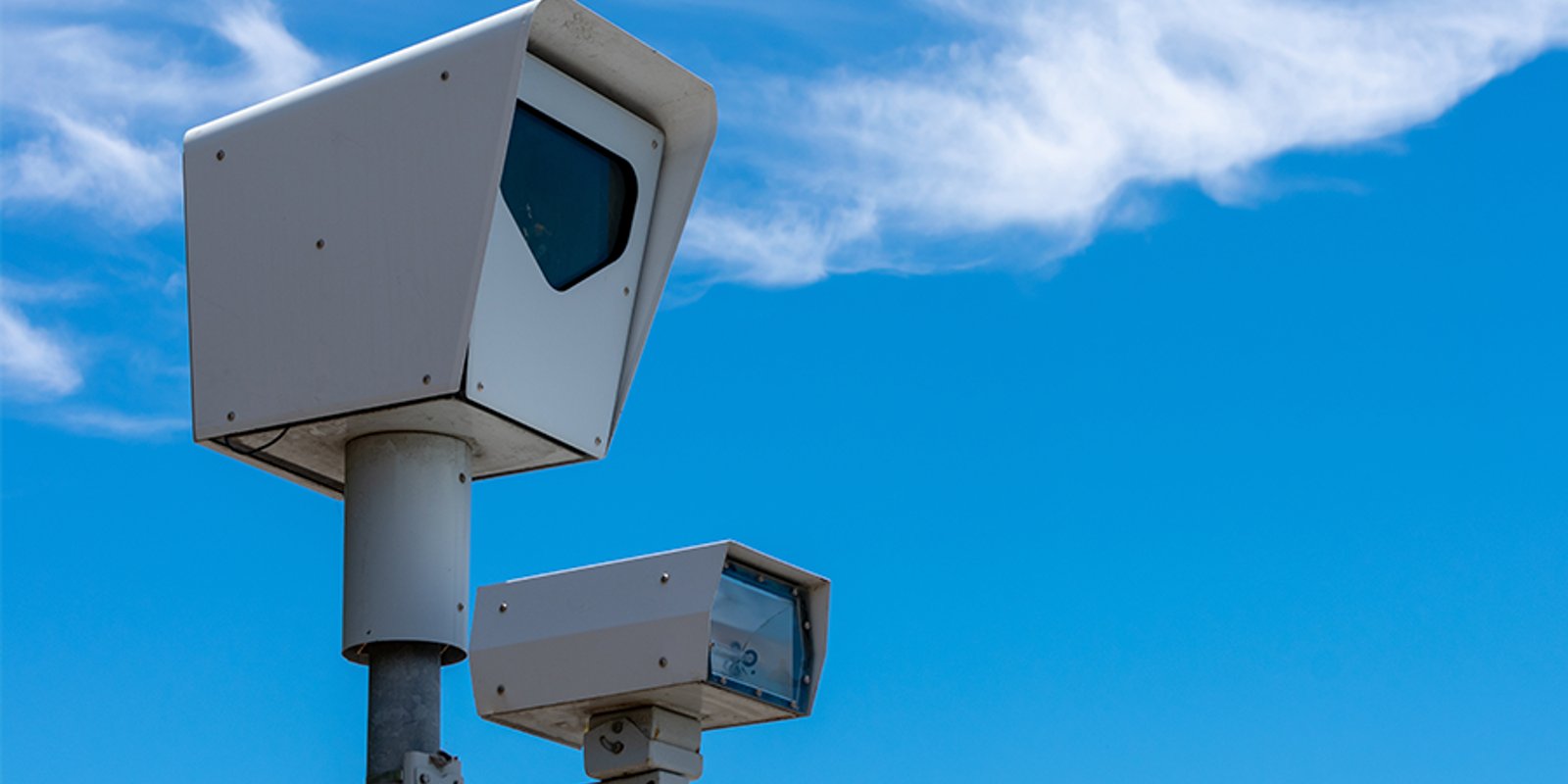 Two white traffic enforcement cameras mounted on a metal pole against a blue sky